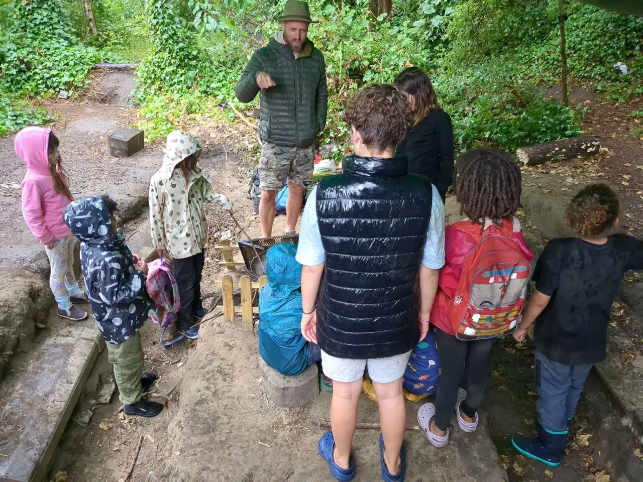 A practitioner crouching to brief a group of children gathered around the fire circle before a session