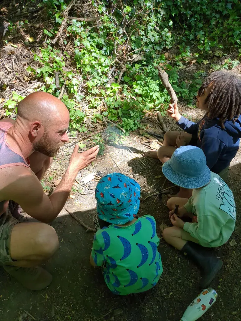 A practitioner crouching to talk with three young children beside a small fire