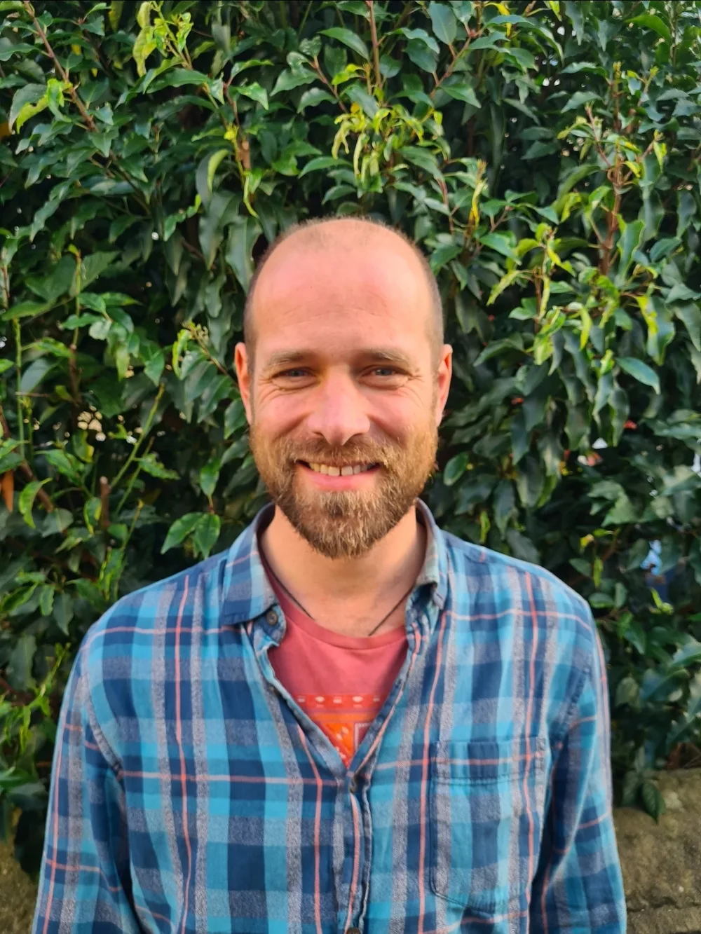 Dan, Founder and Lead Practitioner at Acorn to Oak, smiling outdoors in front of a hedge
